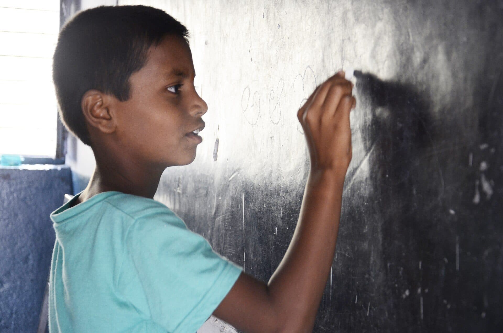 A schoolboy writing on a classroom blackboard